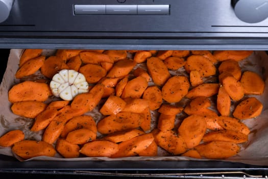 Fresh raw carrots cut into pieces with spices on a baking tray in the oven. Selective focus.