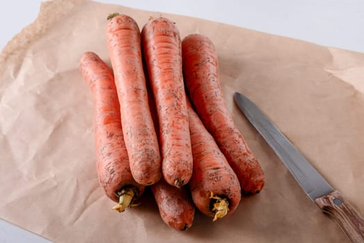 Fresh raw carrots lie on parchment paper on the kitchen table. Selective focus.