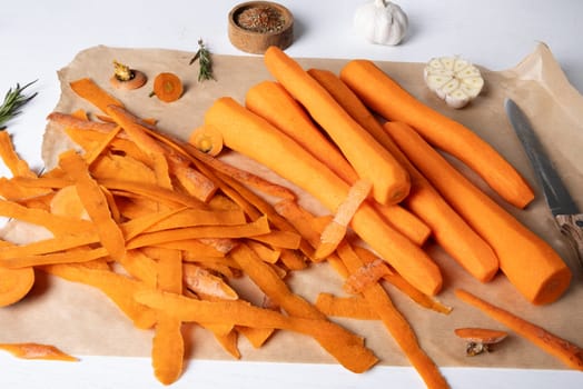 Peeled fresh raw carrots lie on parchment paper on the kitchen table. Selective focus.