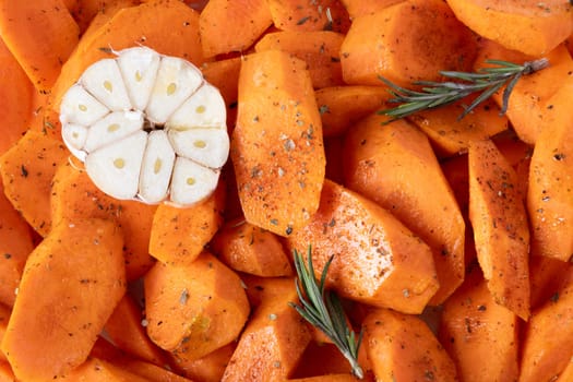 Fresh carrots cut into pieces, seasoned with spices and olive oil, lie on baking tray. Food background. Selective focus.