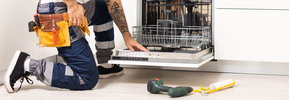 man repairing dishwasher. Male hand with screwdriver installs kitchen appliances, close up.