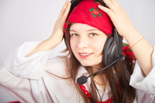 Portrait of young girl in a bright red scarf and large headphones with a microphone. A woman who is radio or television presenter in the workplace. Funny female telecom operator. Freelancer at work