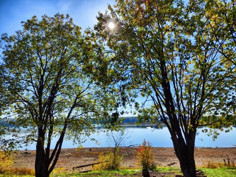 Autumn fall in park with yellow leaves trees and river or lake with blue sky on background in a sunny day