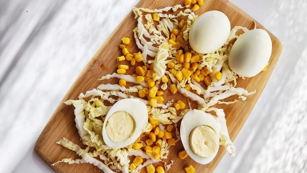 Chopped Peking cabbage, peeled eggs and yellow canned corn on cutting board as background. Cooking a healthy eco-friendly salad from natural products. Copy space and place for text