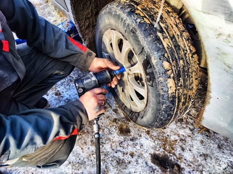 Ishim, Russia - November 27, 2023: man makes tire of car wheel before cold snow season. Experienced mechanic changes wheel of car. The driver prepares a classic car for driving in the snow in winter