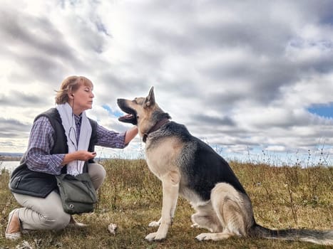 Adult girl with shepherd dog taking selfies in field. Middle aged woman and big shepherd dog on nature. Friendship, love, communication, fun, hugs