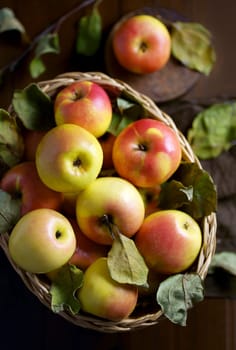 Apples in a basket on a wooden table. Fresh red apples with green leaves on a black background. Fruits.