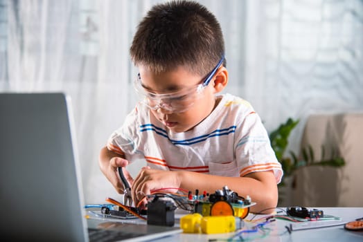 Asian kid boy assembling the Arduino robot car homework project at home, Little child tighten the nut with a screwdriver to assemble car toy, creating electronic AI technology workshop school lesson