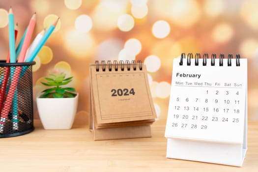 White February 2024 desk calendar on wooden table with gold light bokeh background. New Year Concept.
