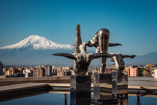 Cityscape with mountain view in the morning time concept photo. Yerevan, capital of Armenia in front of mountain Ararat. Modern art - stainless steel sculptures of three athletes in the pool. High quality picture for magazine, article