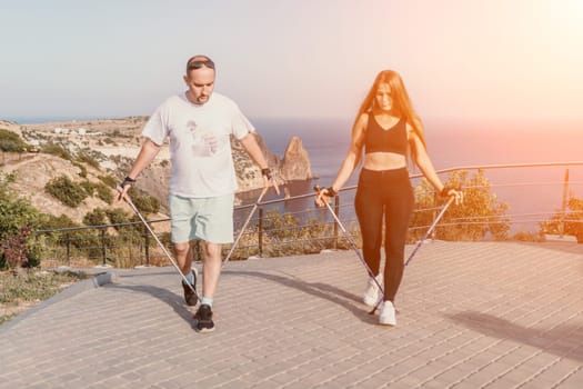 Happy Middle aged couple or friends practicing nordic walking in park near sea. Mature couple with trekking poles walking, practicing Nordic walking outdoors. Aging youthfully and sport concept.