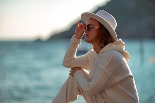 Happy blonde woman in a white suit and hat posing at the camera against the backdrop of the sea.