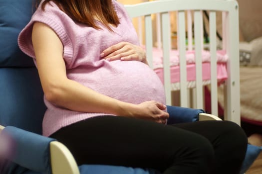 Woman is holding her stomach while sitting in a chair. A pregnant woman is expecting a baby