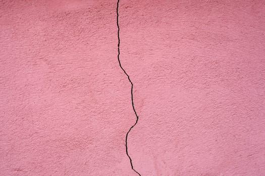 Pink plaster facade house wall with dark cracks. Texture for background.