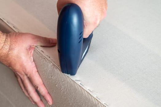 Worker stapling sofa lining with electric staple gun