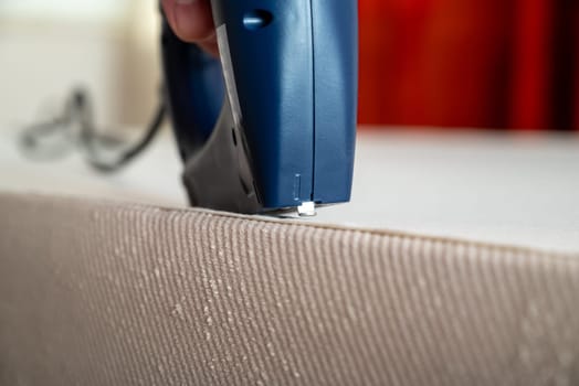 Worker stapling sofa lining with electric staple gun