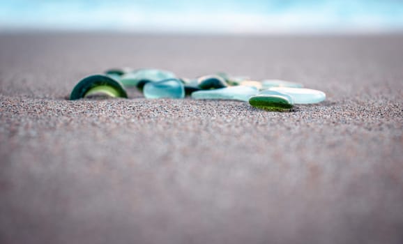 Sand beach and glass stones concept photo. Glass stones from broken bottles polished by the sea. Front view photography with blurred background. High quality picture for wallpaper, travel blog