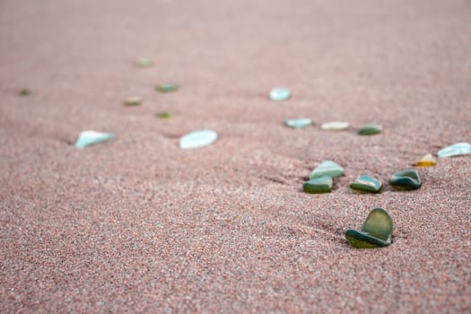 Sand beach and stones with foam concept photo. Glass stones from broken bottles polished by the sea. Front view photography with blurred background. High quality picture for wallpaper, travel blog