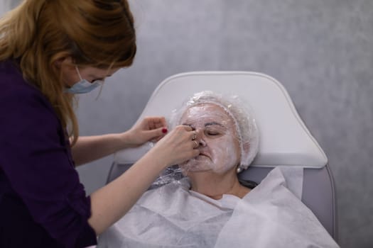 The specialist at the beauty salon wraps the client's facial skin with a film to intensify the effect of the product.
