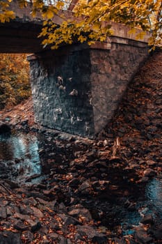 The old bridge over the river of the autumn forest. Forest river stream landscape. Bridge over forest river stream. Beautiful nature scenery photography. High quality picture for wallpaper, travel blog.