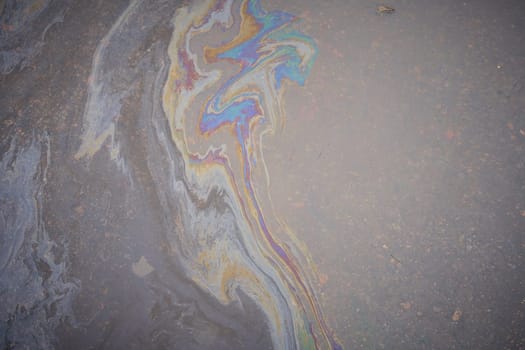 Close-up of an iridescent oil or gasoline spill on a wet asphalt, viewed from above. Bold multicolored spots on the asphalt. Concept of environmental problems