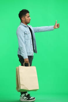 Man on a green background with shoppers show thumb up, in profile.