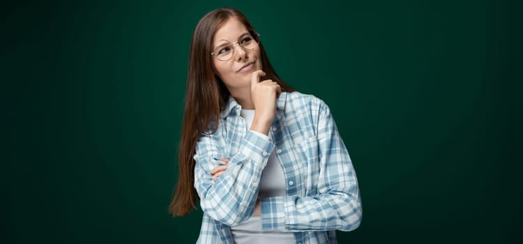 Charming young woman with brown hair thinking on a green background with copy space.