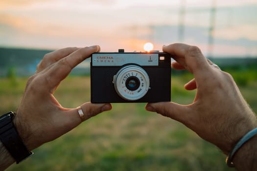 Kyiv, Ukraine - May 2023. Old metal Smena 8 in man hands on sunset background. Soviet manual analog photo camera made in USSR. High quality photo