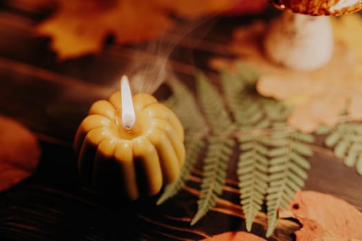 Autumn background. Pumpkin candle, orange fallen leaves. Flat lay. Cozy ambiance of fall, candle burning. Seasonal promotions or tranquil visual storytelling.