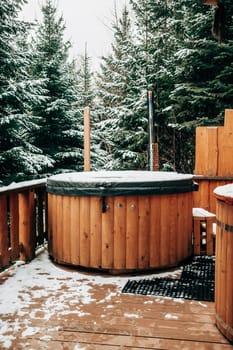 Open-air bath interior near forest, winter, snow view. Wooden hot tub outside. Recreation, spa procedures in steaming pool, private treatment. Thermal at snowy mountains.