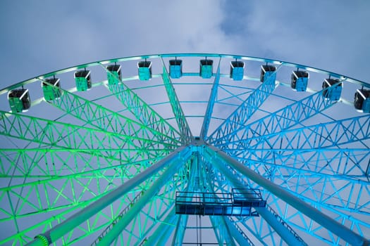 Underside view of colorful ferris wheel over evening sky at amusement park. High quality photo