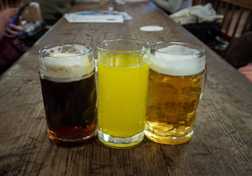 Three glasses of different types of cold tasty beer are in a row on a wooden table in a restaurant. Table for company of friends, Space for text, Selective focus.