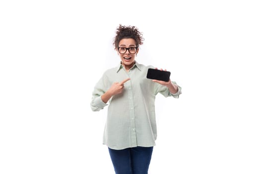 young pretty secretary woman with curly hair dressed in shirt shows smartphone screen with mockup.