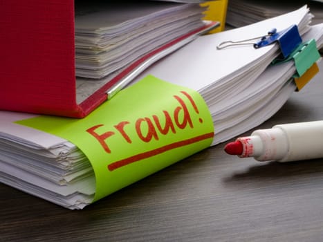 A folder and stack of papers about finances or taxes with an inscription fraud.