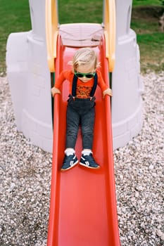 Little girl slides down a slide holding on to the handrails. High quality photo