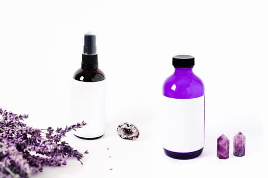 Glass spray bottles on white background surrounded by lavender bouquet and the crystal of quartz. Energy of stones for your home.