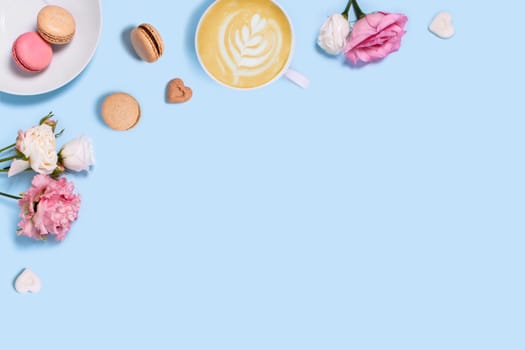 Blue background with macaroons and a cup of coffee surrounded by roses. Top view with space for your text.