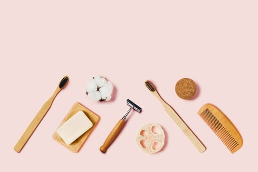 Bathroom accessories on pink background. Natural bamboo toothbrushes, sponges, cotton flowers, shaving brush, razor. Flat lay, top view.