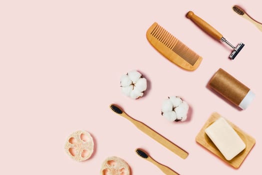 Bathroom accessories on pink background. Natural bamboo toothbrushes, sponges, cotton flowers, shaving brush and soap. Flat lay, top view.