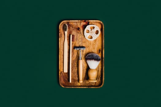 Zero waste concept. Natural bamboo toothbrushes , razor, natural sponge, shaving brush located on wooden tray on green background.