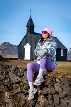 Woman with metallic coat in the black chapel of Budakirkja, Iceland