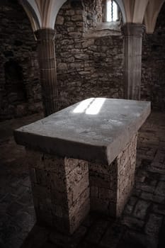 Church interior with columns and altar photo. Remains of monastery interior with arches, medieval city. 11th-century Benedictine monastery photo. Sunlight filtered through the stained glass window. High quality picture for wallpaper, article