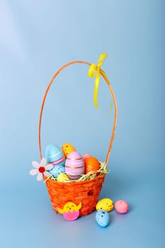 Wicker basket filled with decorative multi colored easters eggs on a light blue background.
