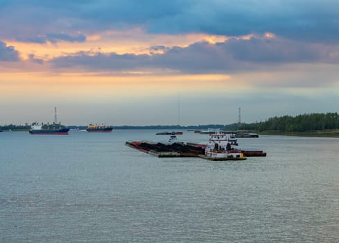 Dramatic sunset over river barge carrying coal down the Mississippi river in Baton Rouge Louisiana looking towards Port Allen