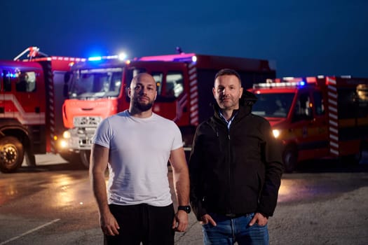 Group of firefighters, dressed in civilian clothing, stand in front of fire trucks during the night, showcasing a moment of camaraderie and unity among the team as they reflect on their duties and the challenges faced during their firefighting service.