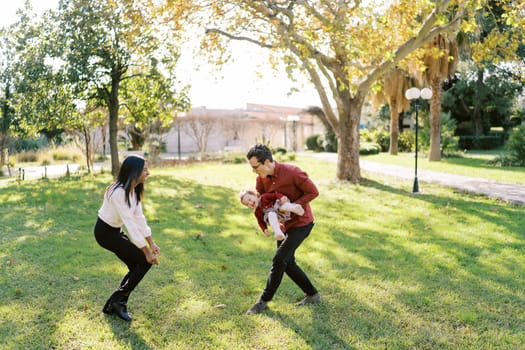 Dad with a little girl in his arms runs to a laughing mom in the park. High quality photo