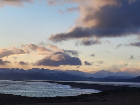 Colorful icelandic wilderness with beach at sunset, golden hour hitting light over rocky mountain slopes in distance. Beautiful landscape capturing frosty natural highlands, winter wonderland.