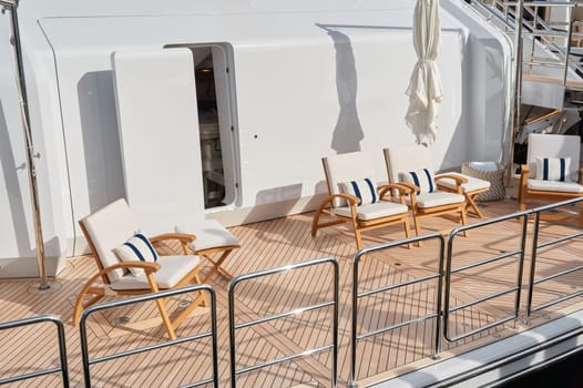 Close-up view of a relaxation area on the open teak deck of an expensive mega yacht at sunny day, with awnings stretched over the deck to protect from the sun, wealth life, table and chairs. High quality photo