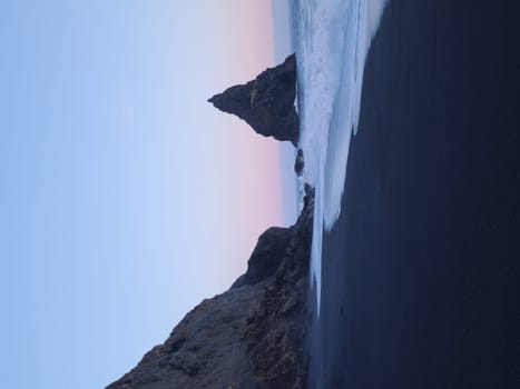 Reynisfjara rock formations on beach with black sand and pink sky near reynisfjall mountain, unique ocean coastline. Amazing stones on shoreline forming natural icelandic landscape, wonderland.