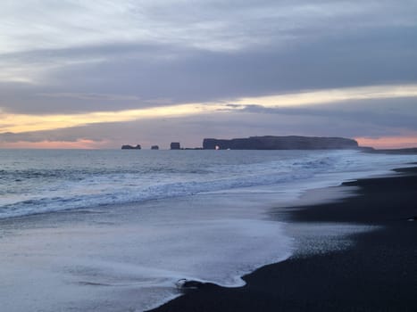 Natural black sand beach at sunset, spectacular coastline with waves crashing on atlantic ocean seashore. Icelandic wintry scenery with huge tides and freezing cold water, nordic nature.